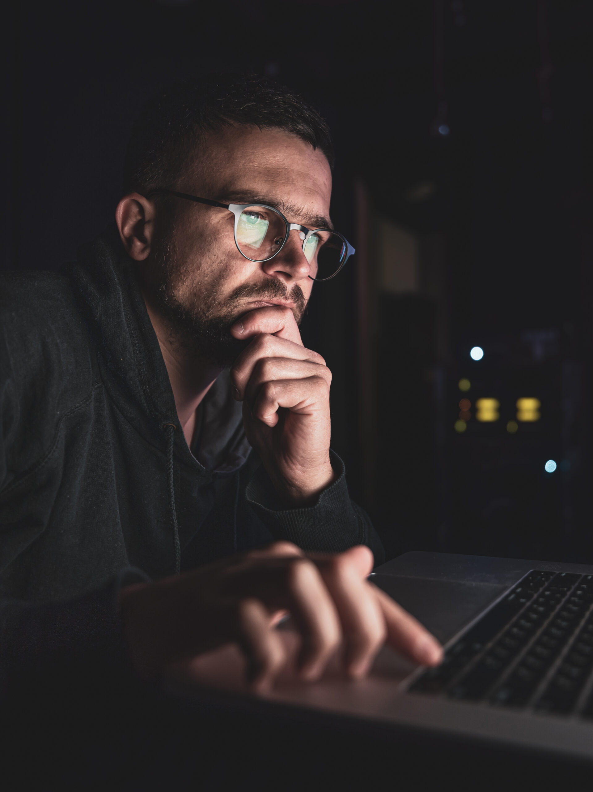 A man with glasses in the dark looks at the computer screen, copy space.